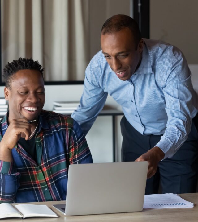 Two colleagues smiling and collaborating on a laptop in an office setting.