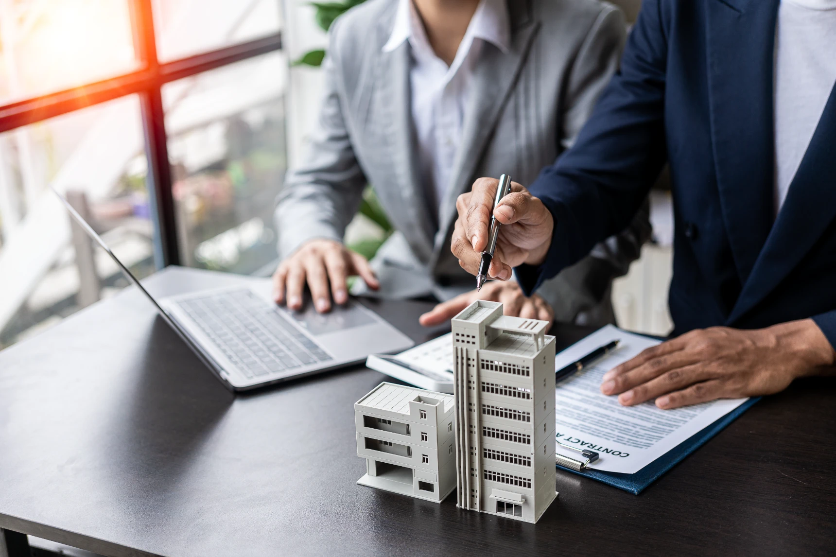 Real estate agents offer contracts to buy or rent housing. Businessman holding model small building house with property insurance at table in home sales office